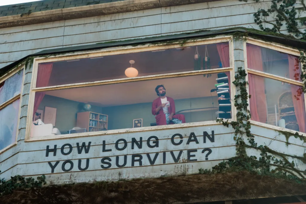 A man in a red robe sits in a fully furnished living room built into a billboard that reads, 