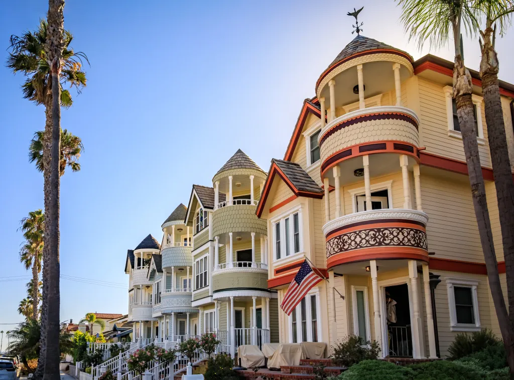 Ornate Victorian houses line a street with palm trees in Huntington Beach, California.