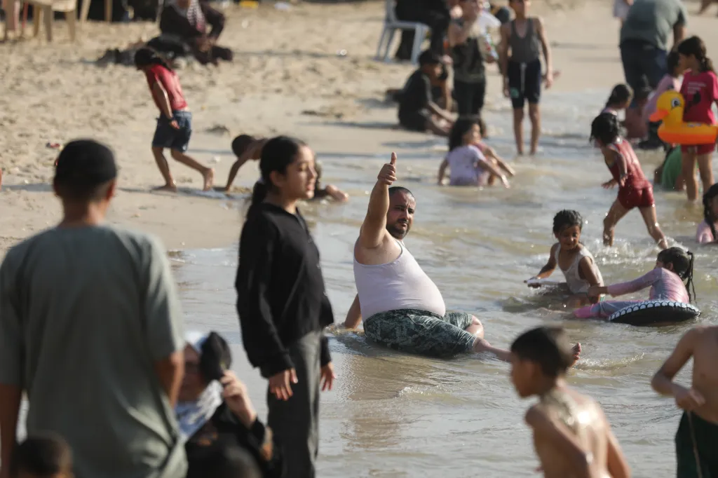 Palestinian families on the beach seeking relief from the summer heat, with adults and children playing in the water.