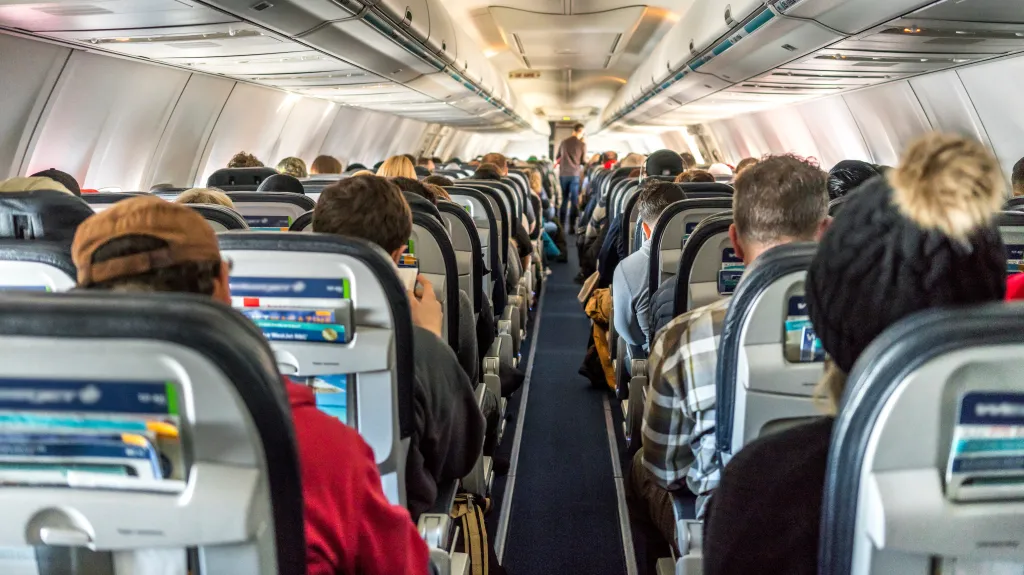 View from inside an airplane cabin looking down the aisle with passengers seated on both sides.