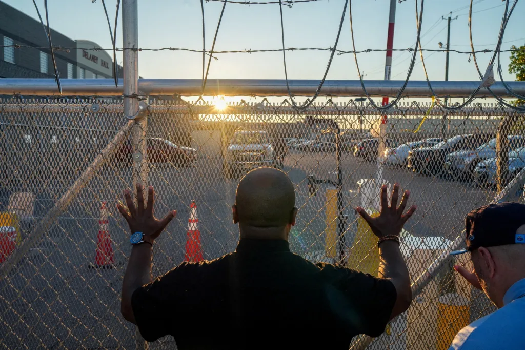 A pastor holds his hands to a gate outside of Delaney Hall detention center on Tuesday, Aug. 4, 2026, in Newark, New Jersey.