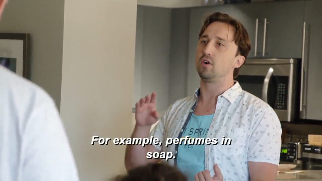 A man wearing a patterned short-sleeved shirt and a light blue t-shirt speaks with text overlayed,