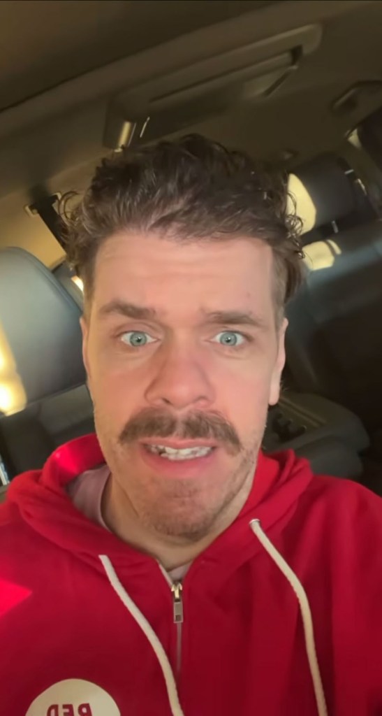 Perez Hilton in a red hoodie and a mustache, with wide eyes and an open mouth.