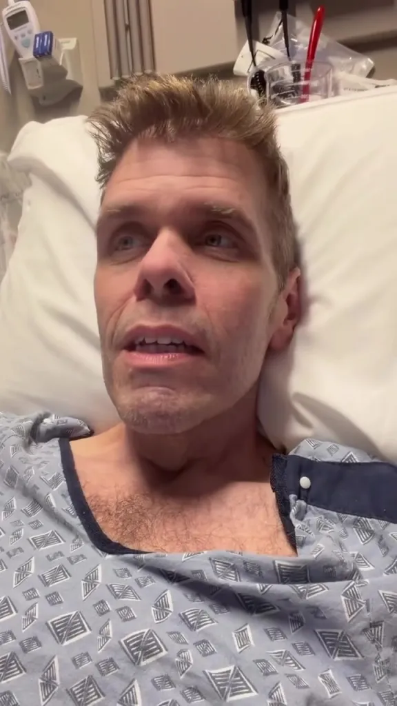 Perez Hilton in a hospital bed, wearing a hospital gown.