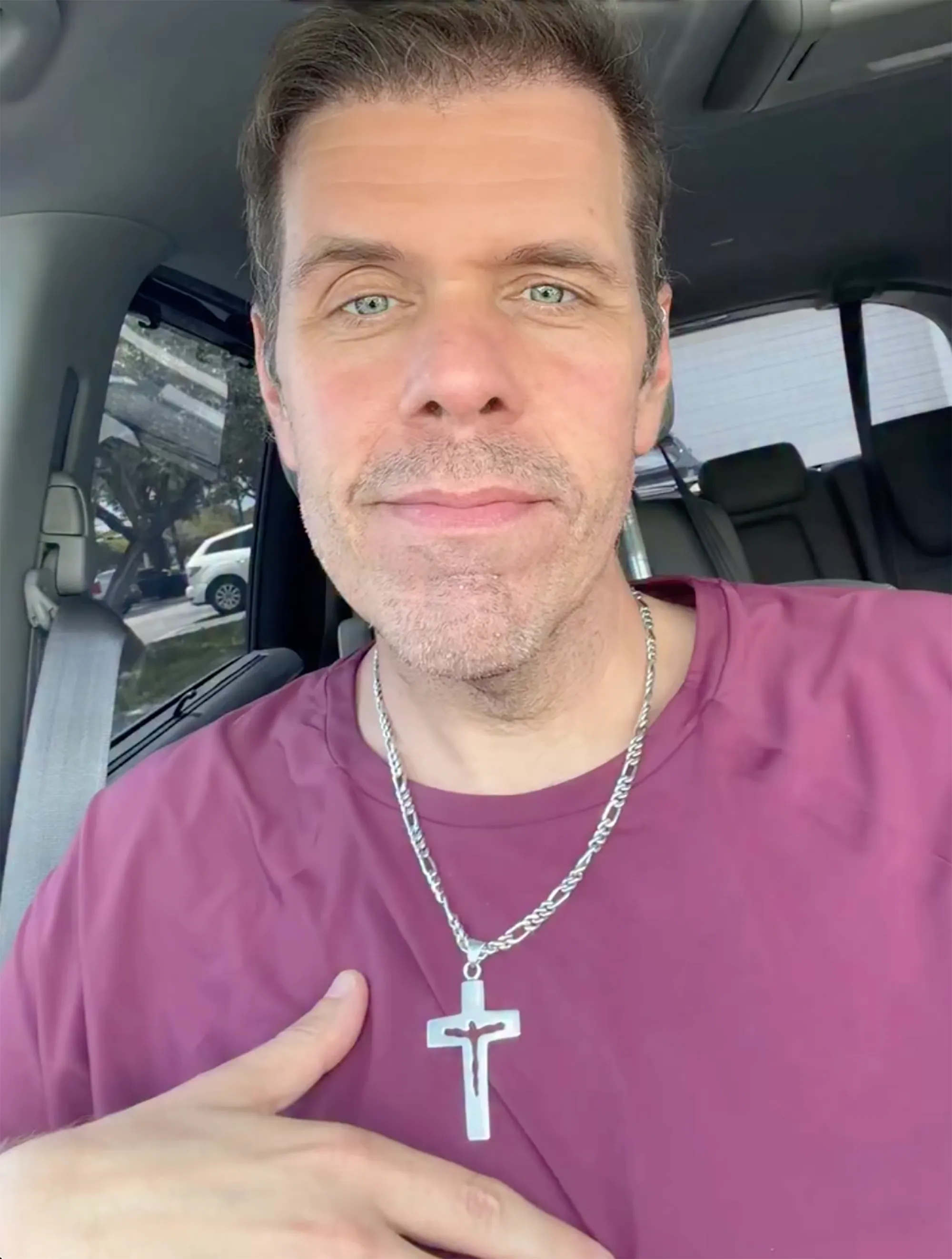 Perez Hilton wearing a maroon shirt and a silver cross necklace.