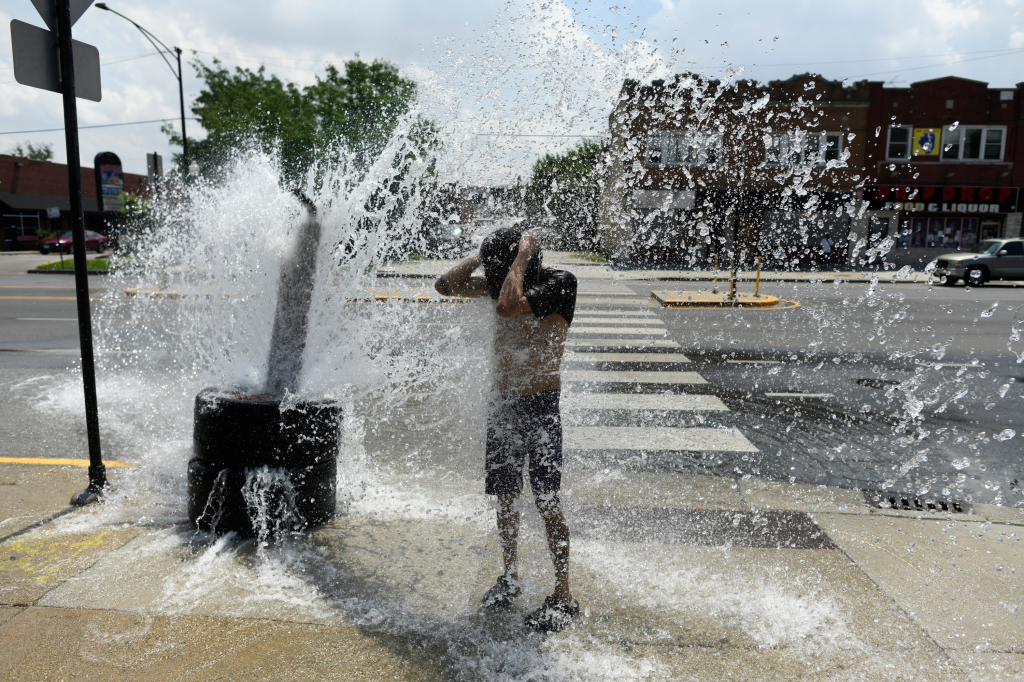 A person cools off with water from an open fire hydrant.