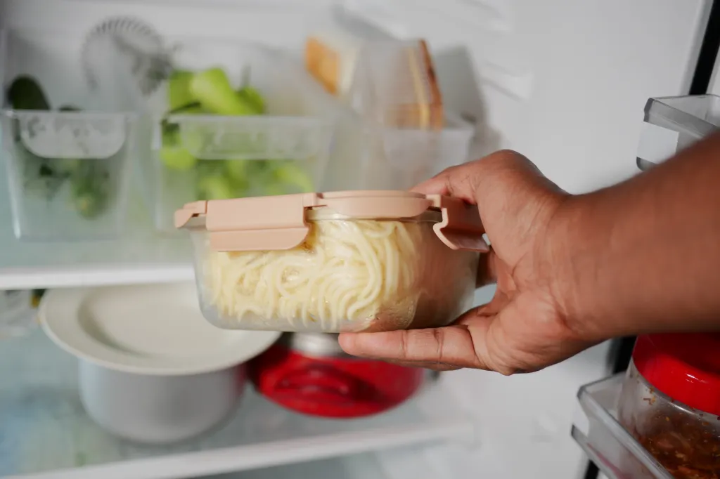 Hand removing a container of spaghetti from a fridge.
