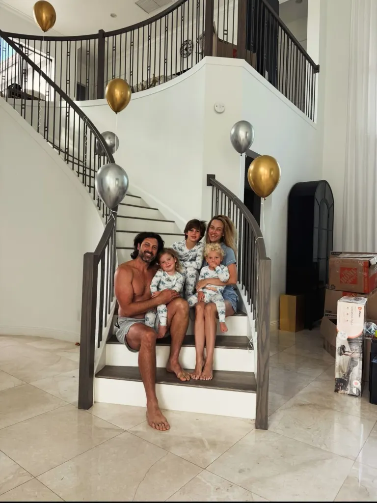 Peta Murgatroyd, Maksim Chmerkovskiy, and their three children sit on a staircase with golden and silver balloons.