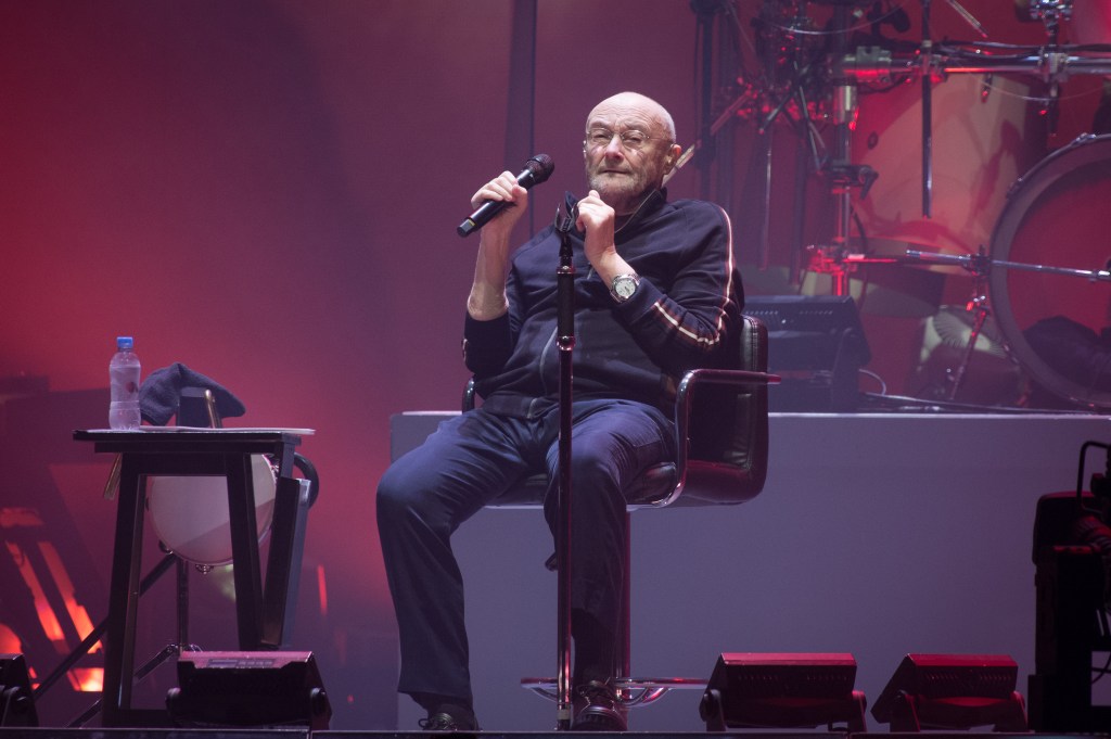 Phil Collins performing while seated and holding a microphone.