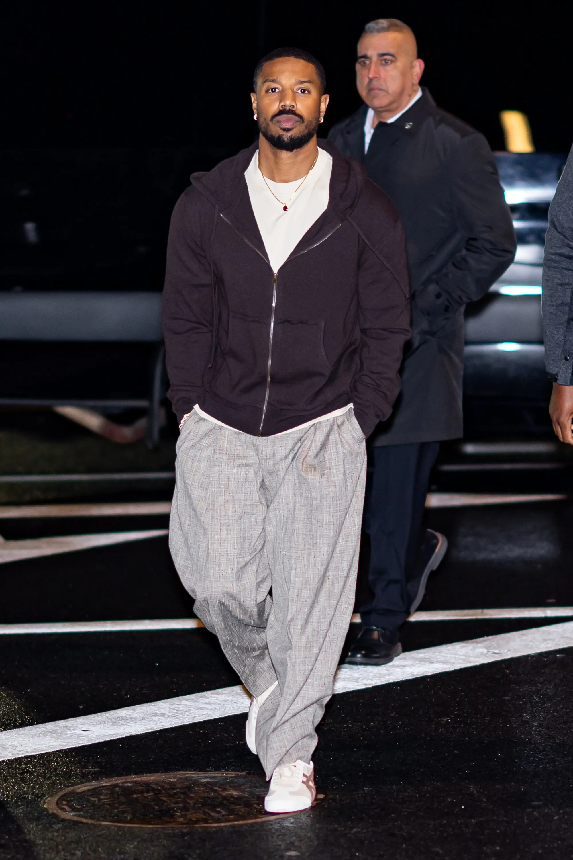 Michael B. Jordan walking outside at night, with a man in the background.