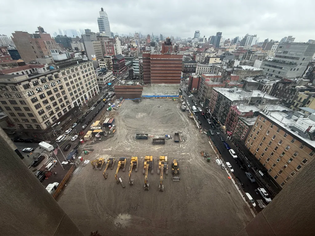 Overhead view of the Manhattan Detention Complex site cleared for new jail construction, with surrounding city buildings and streets visible.
