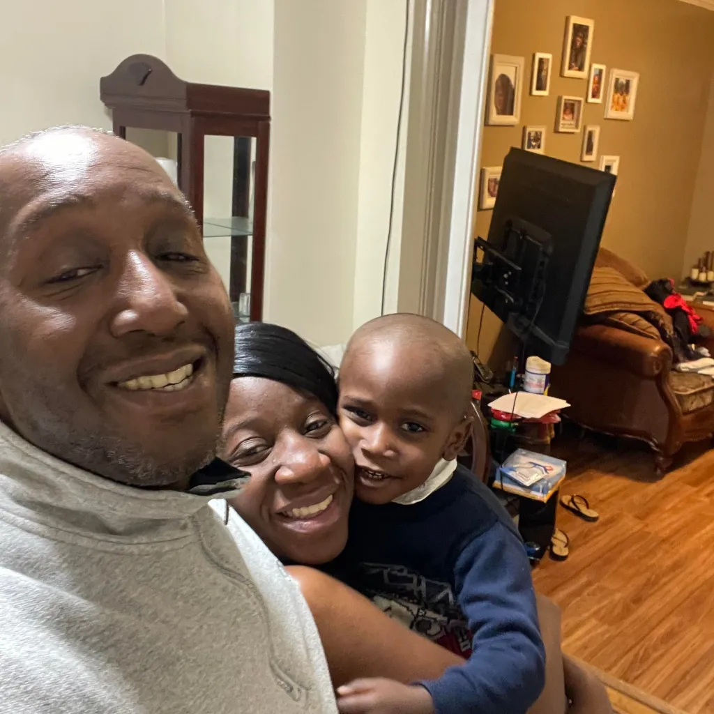 Dimone Fleming, a man, and a child smiling at the camera from their home.