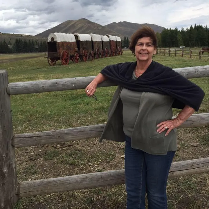 Nancy Guthrie standing next to a wooden fence with covered wagons in the background.