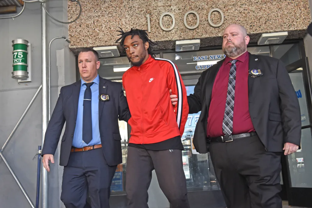 Justin Williams, in a red sweatshirt, is escorted by two officers from the 75th Precinct.