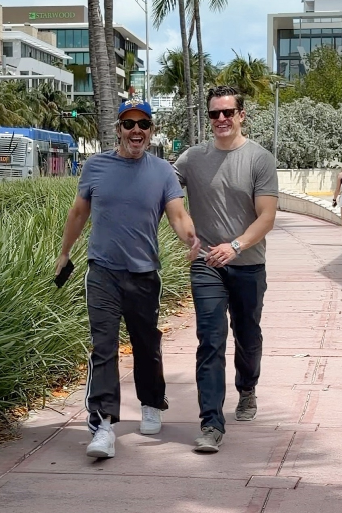 Andy Cohen and Kevin Sobieski smiling and walking together on a Miami street.