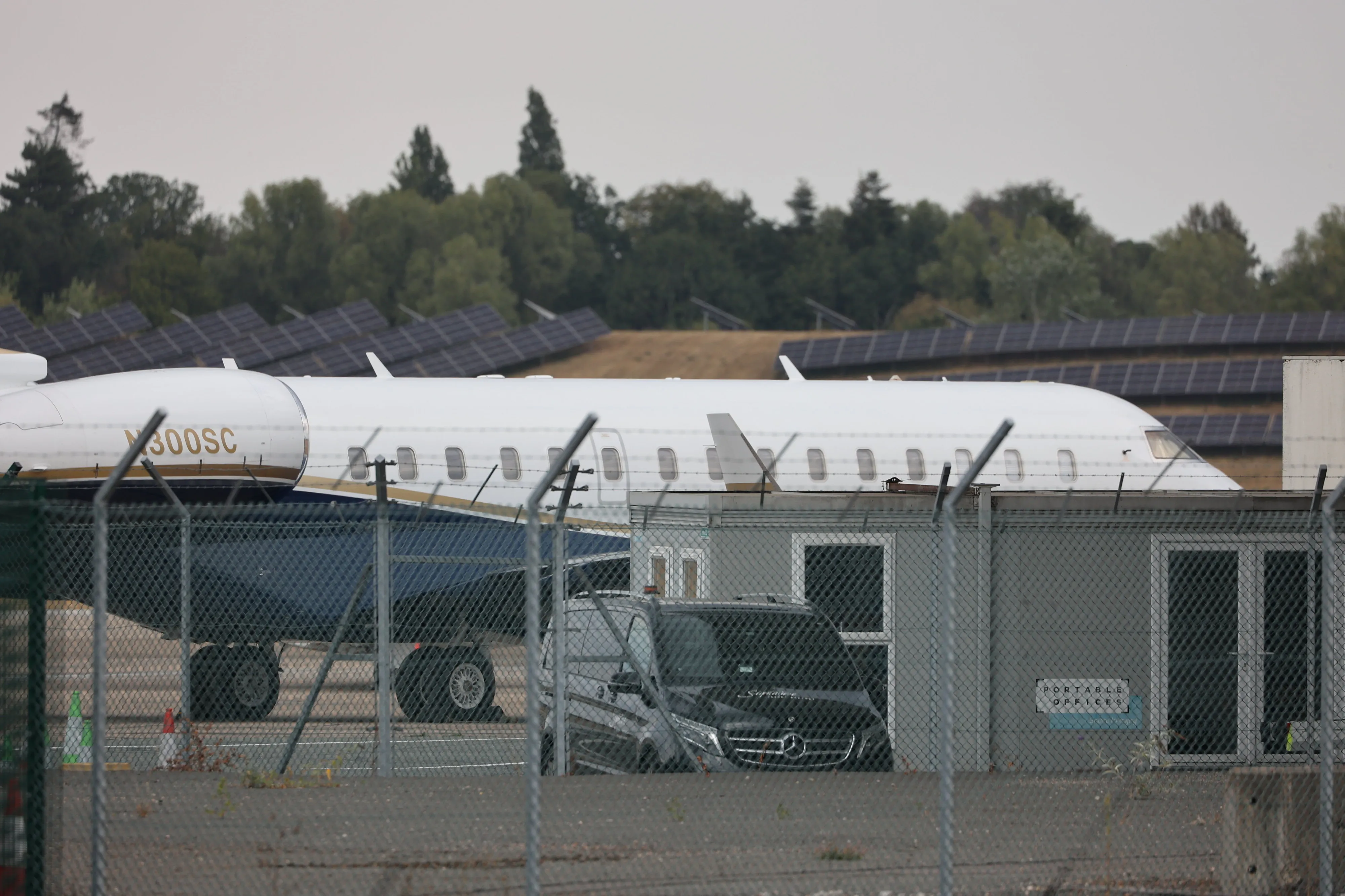A white private jet at Birmingham Airport, with solar panels and trees in the background.