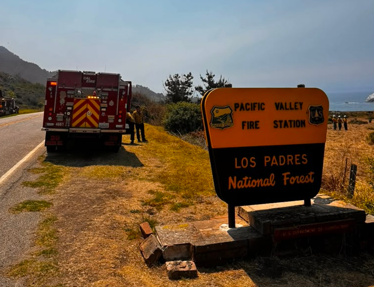 A red fire truck and firefighters on the side of a road in Los Padres National Forest with the ocean in the background.