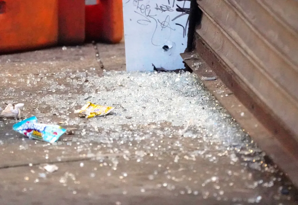 Shattered glass and candy wrappers on the ground in front of a metal barrier.