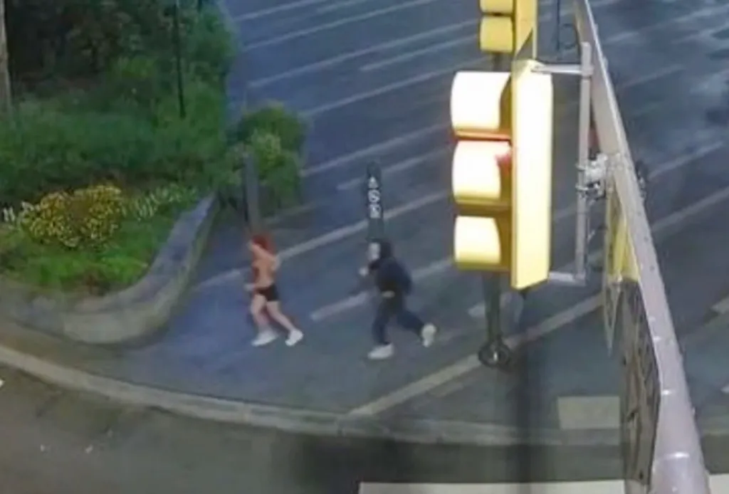 A jogger running past a person in a Chucky doll mask on a street.