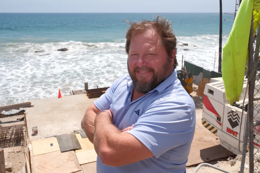 Carl Randall, who is rebuilding his home after it was destroyed by the LA wildfires, smiles with the ocean in the background.