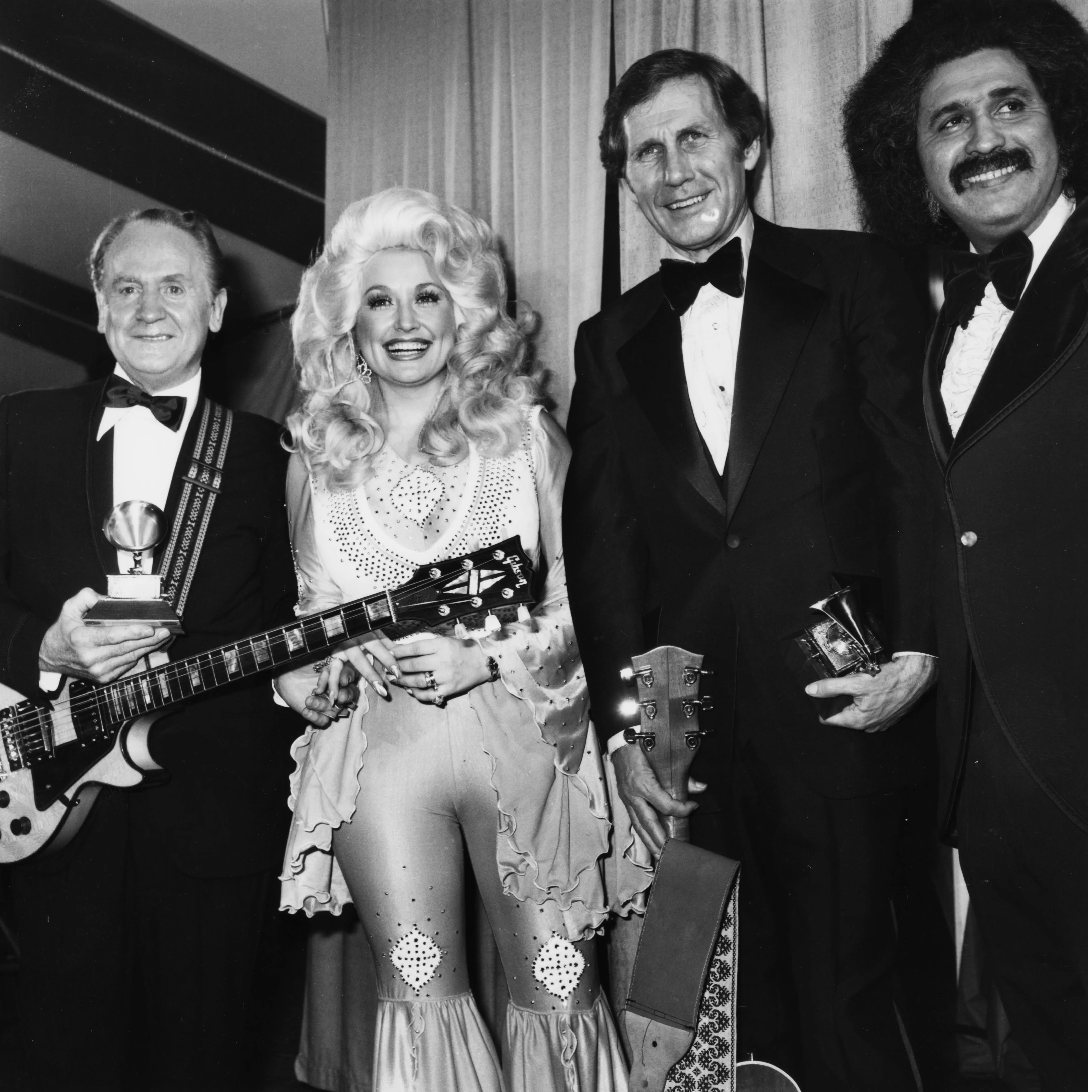 Les Paul, Dolly Parton, Chet Atkins, and Freddie Fender pose together at the 19th Annual Grammy Awards.