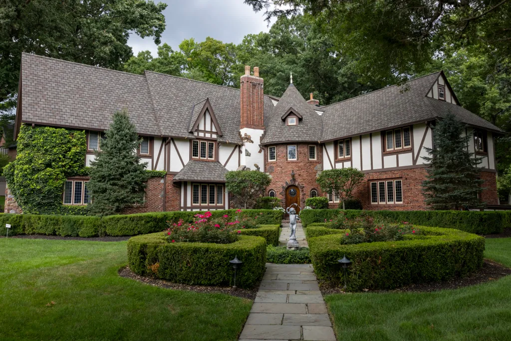 The home of Laura Overdeck at 35 Kenilworth Dr. in Millburn, NJ, a large Tudor-style house with brick and timber-frame detailing, and a manicured front garden with hedges and flowers.