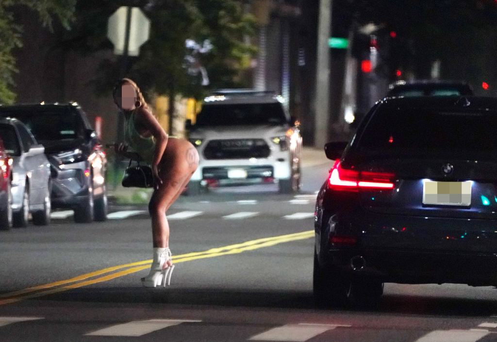 Woman in white boots leaning into a car on a street at night.