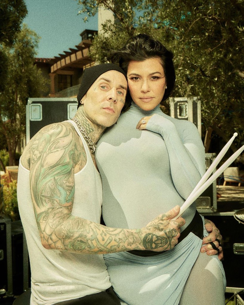 Pregnant Kourtney Kardashian and Travis Barker embrace, with Barker holding drumsticks.