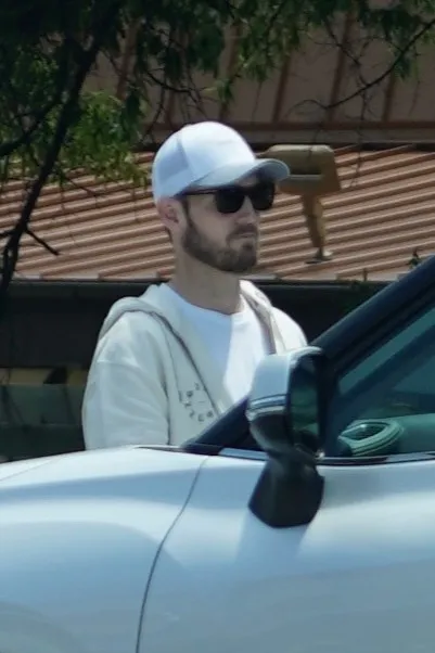 Brian Hickerson wearing a white hat and sunglasses, looking out of a white car.