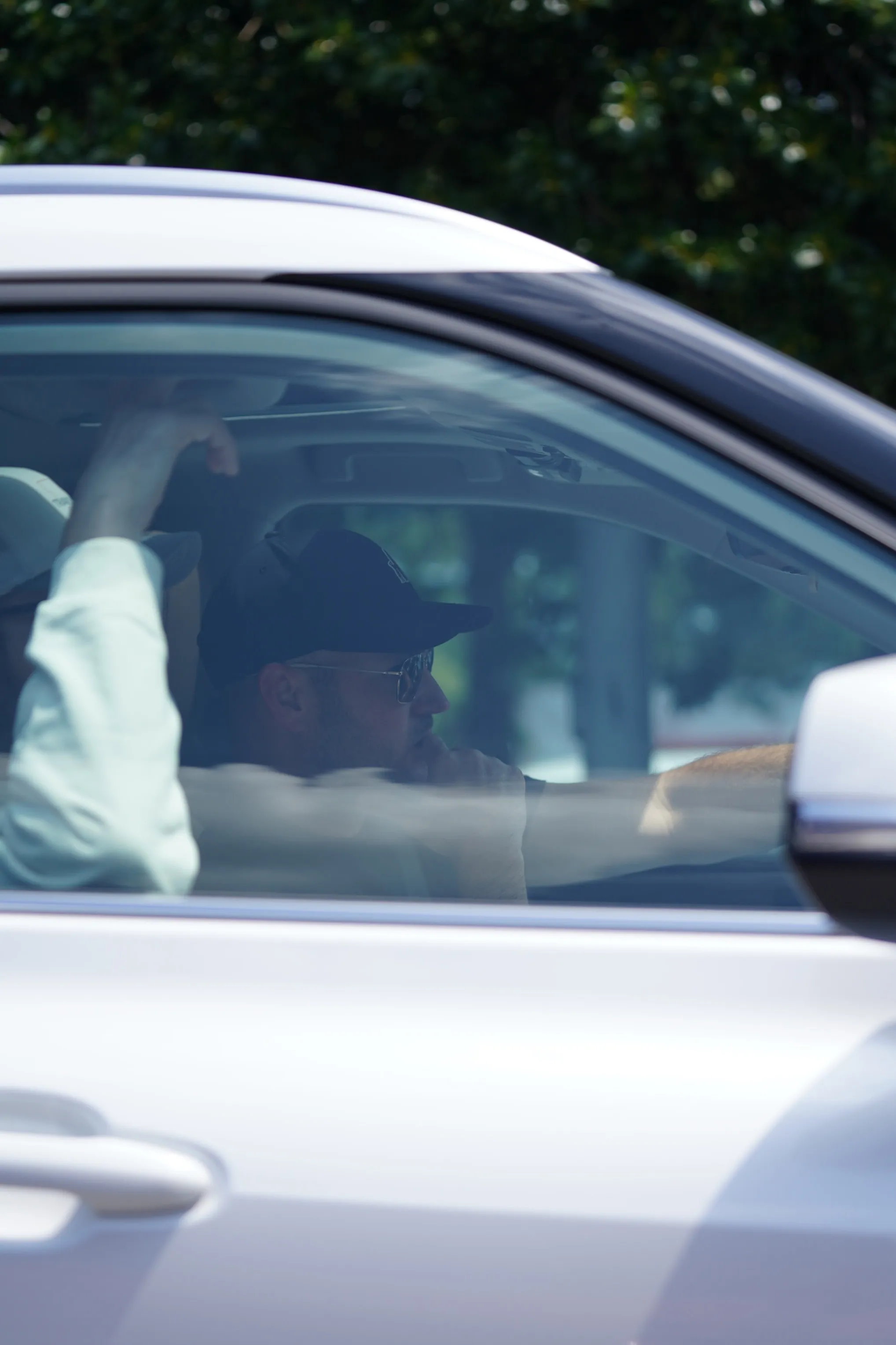 Brian Hickerson wearing a cap and sunglasses, sitting in the passenger seat of a car.