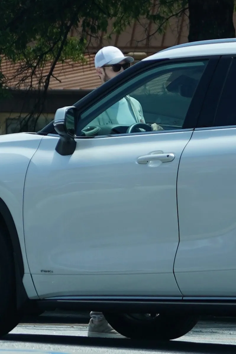 Brian Hickerson in a white baseball cap and sunglasses sitting in the driver's seat of a white car.