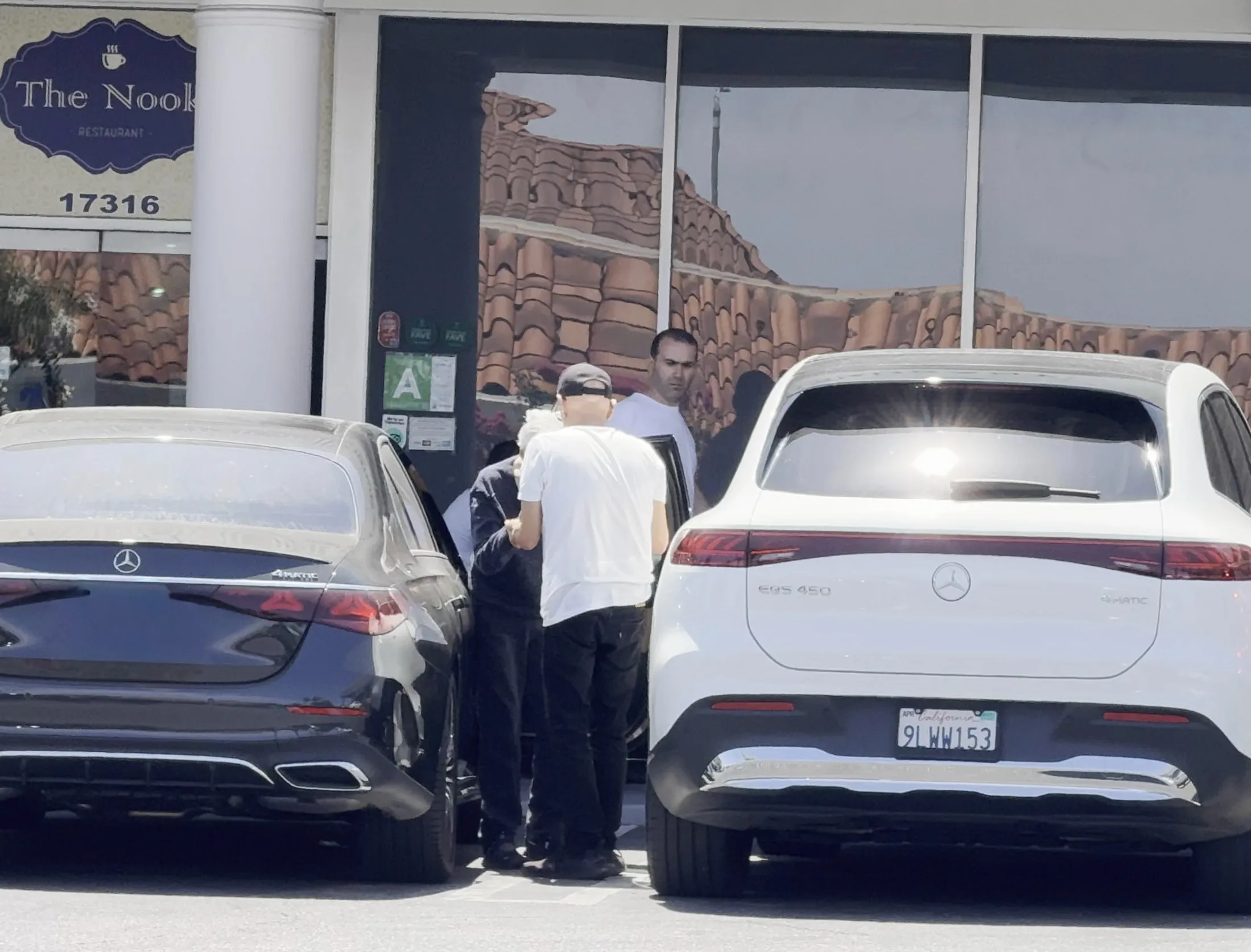 Frankie Valli in a wheelchair with a caretaker, exiting a black car in front of 