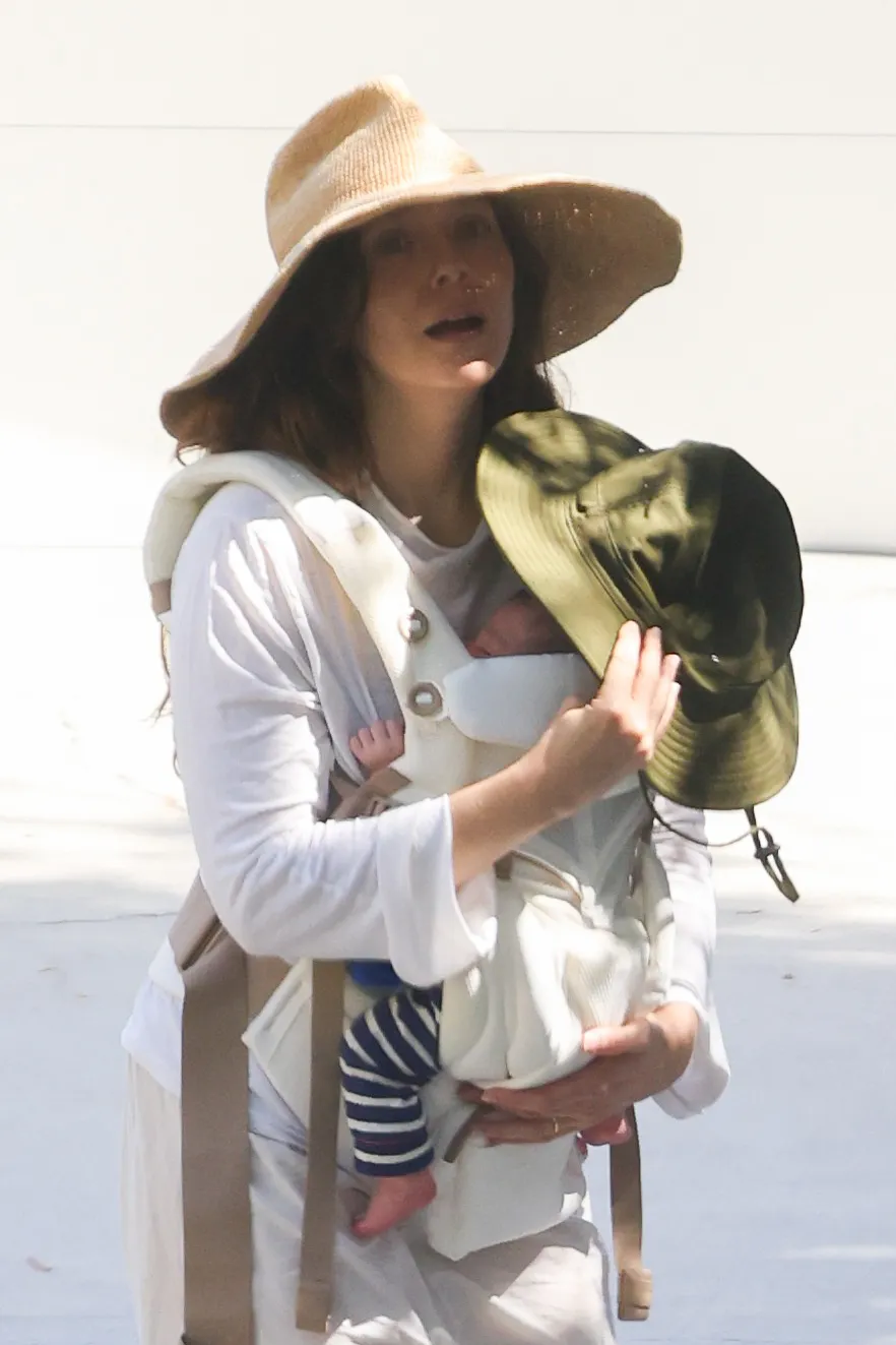 Elizabeth Olsen carrying her newborn baby in a carrier while wearing a straw hat.