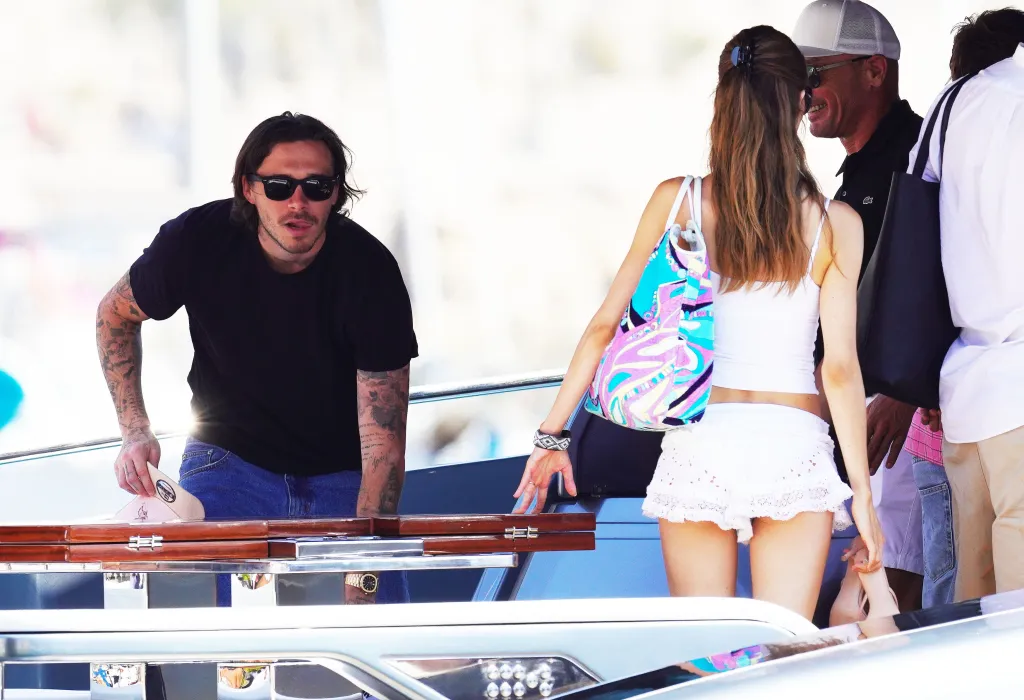 Brooklyn Beckham carrying a hat and looking towards a group of people, including his wife Nicola Peltz, on a yacht in Saint-Tropez.