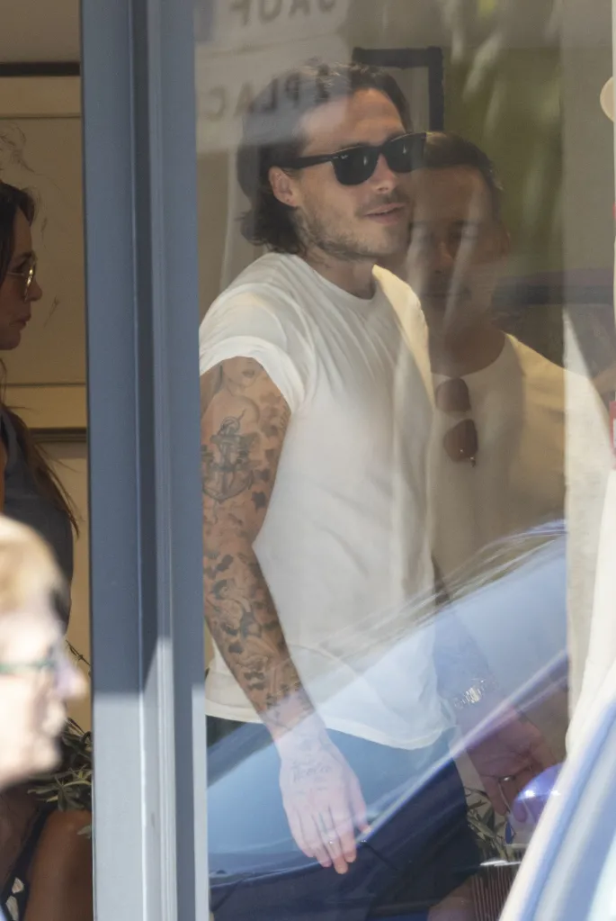 Brooklyn Beckham wearing sunglasses and a white t-shirt, looking out through a window.
