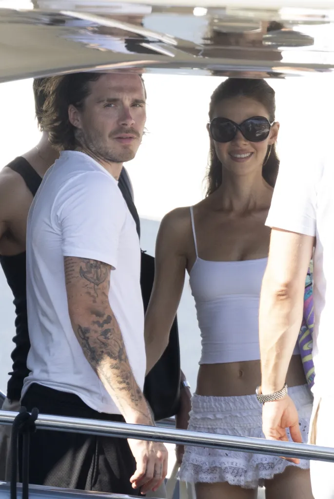 Brooklyn Beckham and Nicola Peltz standing together, with Peltz wearing sunglasses and smiling.