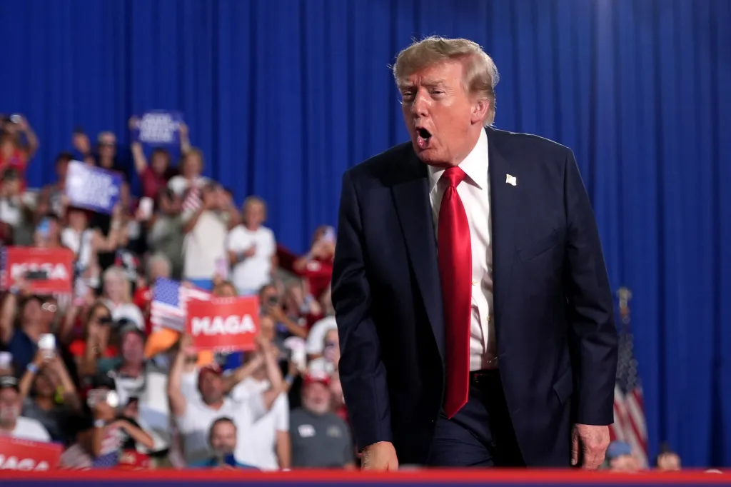 President Donald Trump speaking to a crowd with supporters holding 