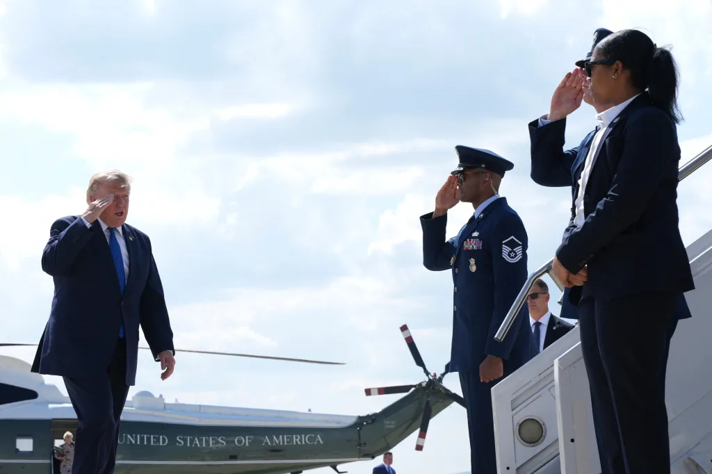 Donald Trump salutes while walking towards Air Force One, as two service members also salute.