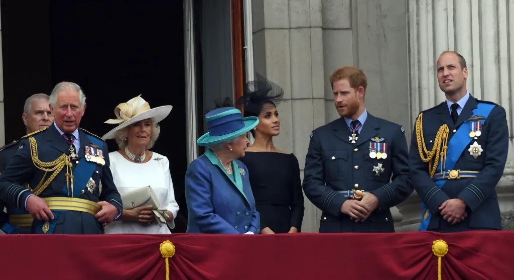 British Royal family members on a balcony, including Prince Charles, Camilla, Queen Elizabeth II, Meghan, Prince Harry, and Prince William.