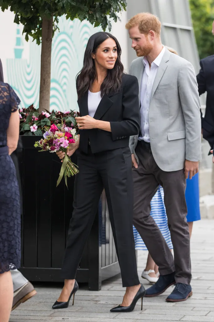 Meghan Markle, Duchess of Sussex, and Prince Harry, Duke of Sussex, walking together, with Meghan holding a colorful bouquet of flowers.