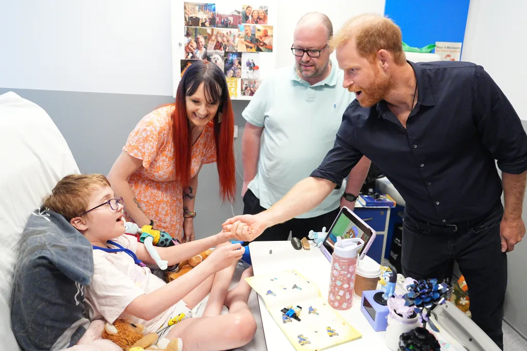 Prince Harry, in a black shirt and black jeans, holding hands with patient Alec Hill as his parents Kelly and Stuart Hill look on during a visit to Birmingham Children's Hospital.