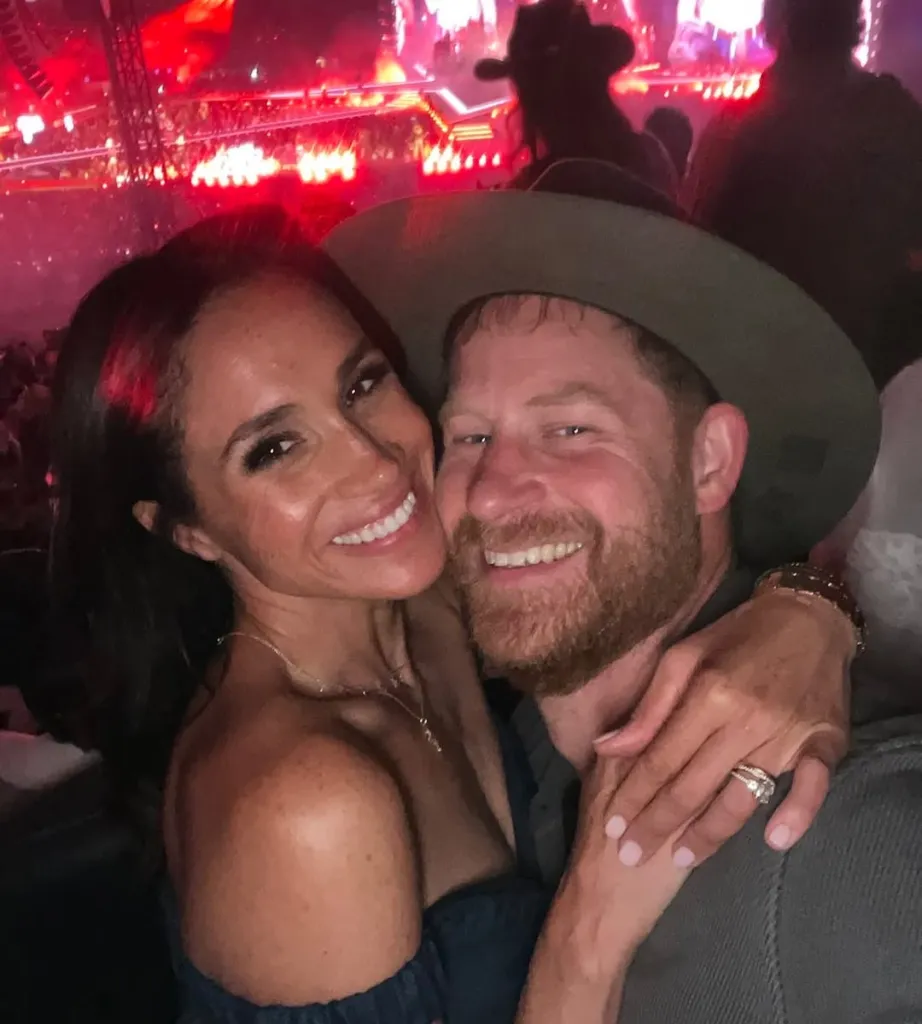 Meghan Markle with her arm around Prince Harry, who is wearing a cowboy hat, both smiling at a concert.