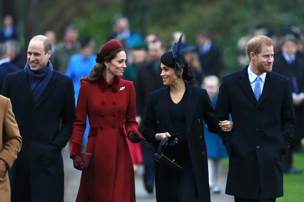 Prince William, in a black coat and blue scarf, Kate Middleton, in a red coat and red hat, Meghan Markle, in a black dress, black coat and black hat, and Prince Harry , in a black coat, blue shirt and blue tie, walking together, dressed in winter coats.
