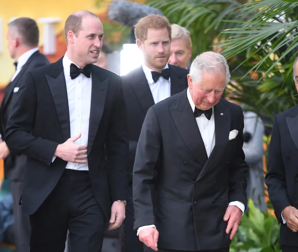 Prince William, Prince Harry, and Prince Charles in tuxedos on a red carpet.