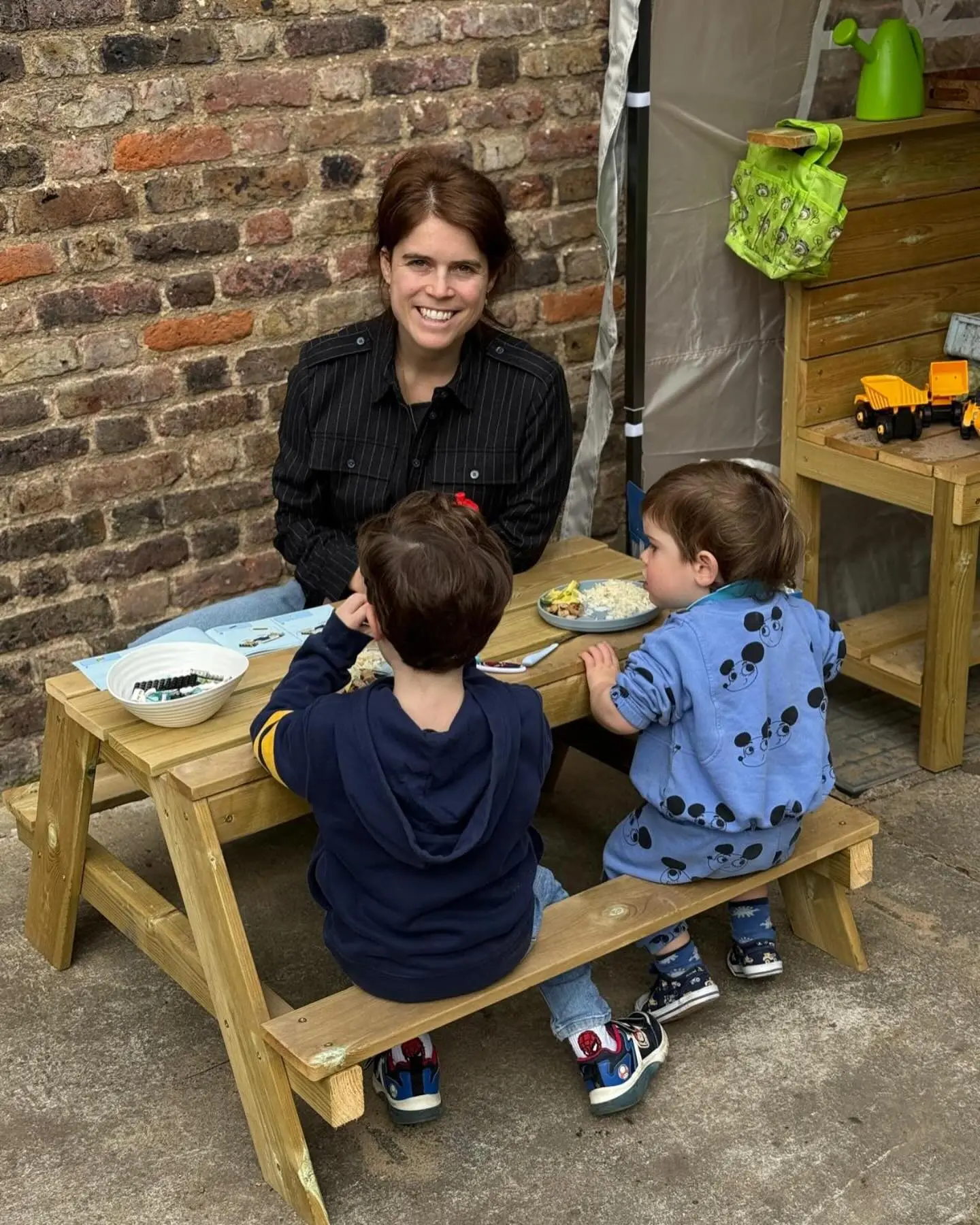 Princess Eugenie smiling at a picnic table with two young children.