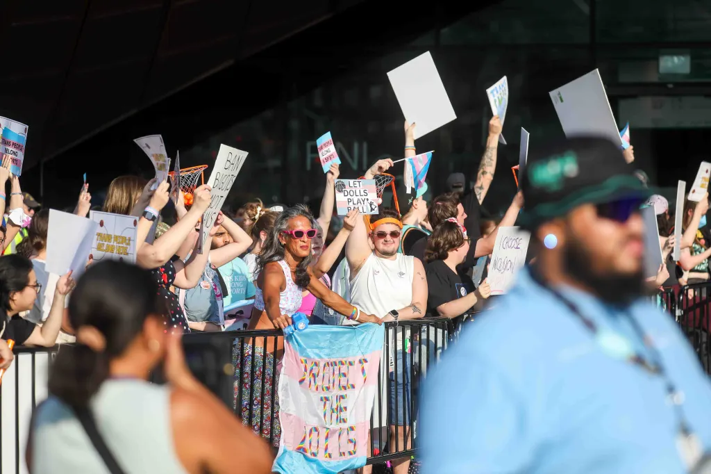 Pro-trans inclusion protestors hold signs and a trans flag.