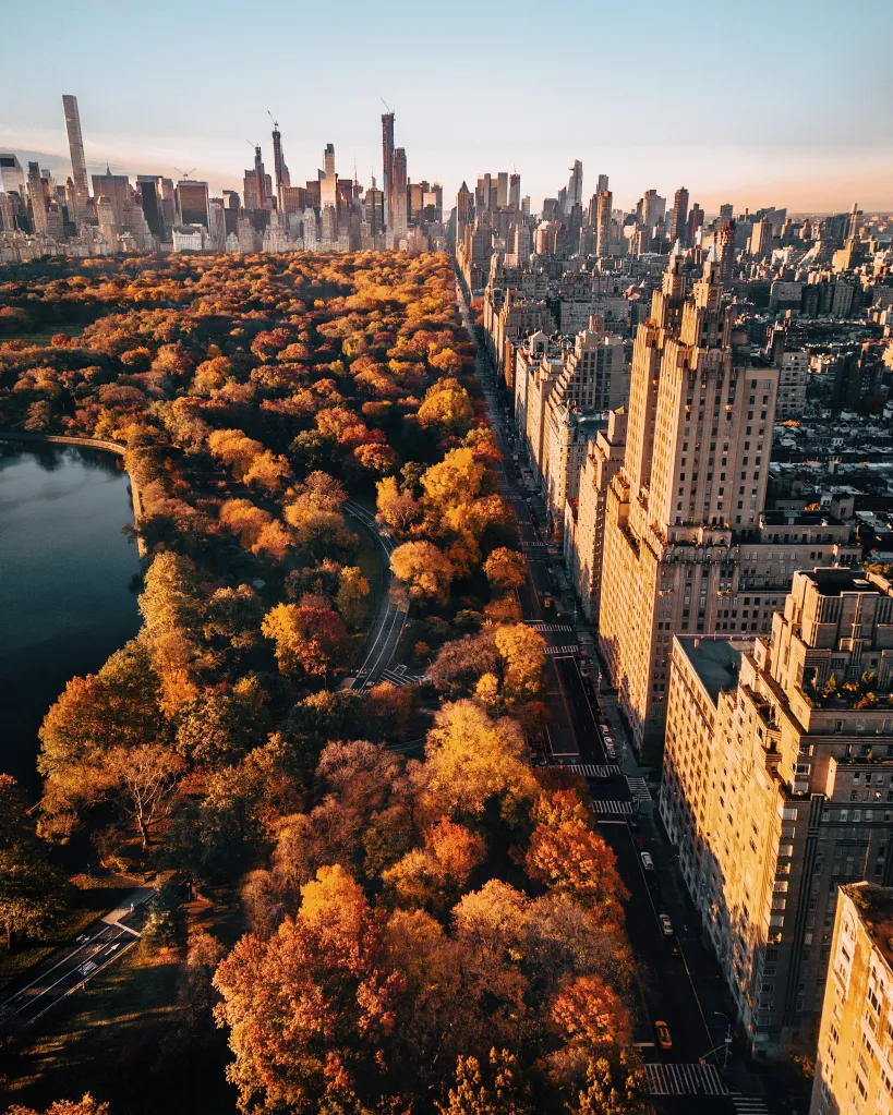 Aerial view of Central Park in autumn, with a lake and fall foliage, bordering the Upper West Side buildings in New York City.