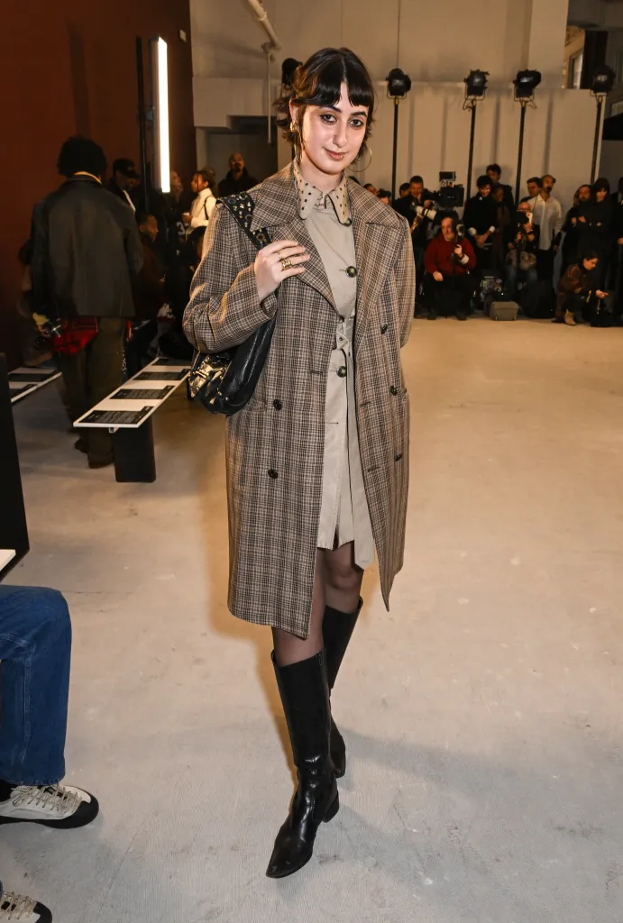 Rama Duwaji in a plaid coat and black boots at the Diotima fashion show.