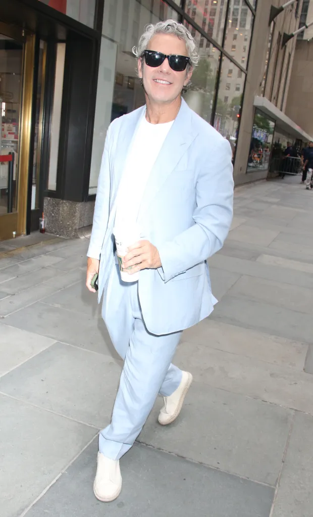 Andy Cohen in a light blue suit and sunglasses, holding a coffee cup, outside the Today Show.