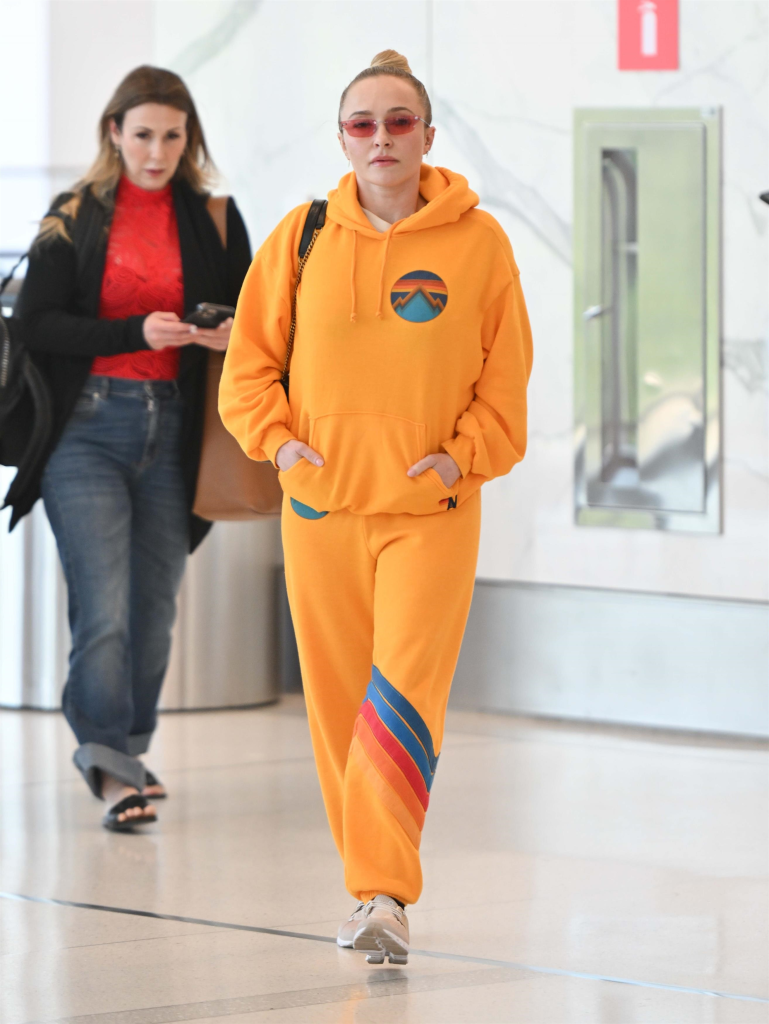 Hayden Panettiere in a bright orange hoodie and sweatpants with Kasey Kitchen walking through LaGuardia Airport.
